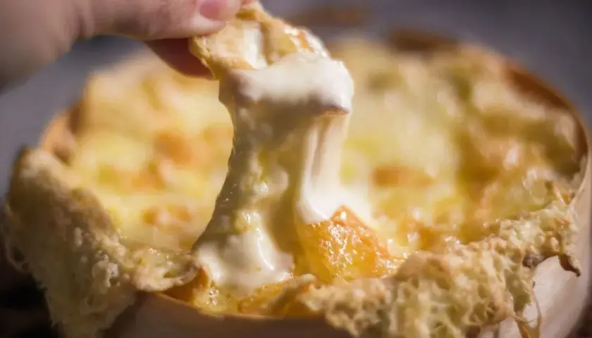 Un morceau de pain trempé dans un fromage fondu doré, prêt à être dégusté. Une invitation à découvrir la recette du Berthoud.