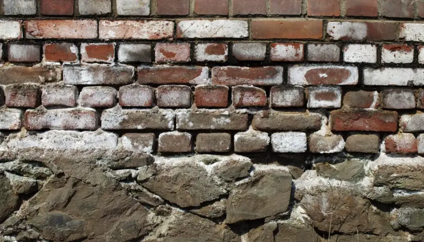 Alte Ziegelwand mit deutlichen Spuren von Salpeter. Die unteren Steine sind grob behauen und bilden eine solide Basis.