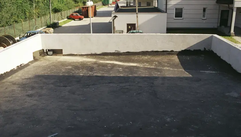 Widok na płaski dach z widocznymi etapami odwodnienia. W tle budynki i drzewa.