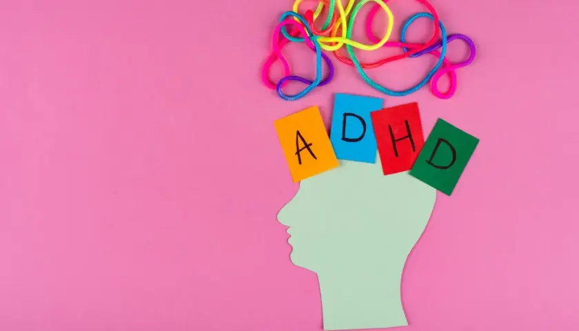 Kolorowe sznurki nad głową symbolizują chaos myśli. Kartki z literami A, D, H, D układają się w napis ADHD.