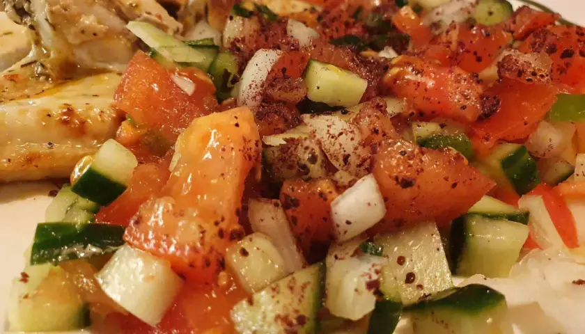 En saftig coban salata med tomater, gurka och lök, kryddad med sumak, serveras bredvid grillad kyckling.