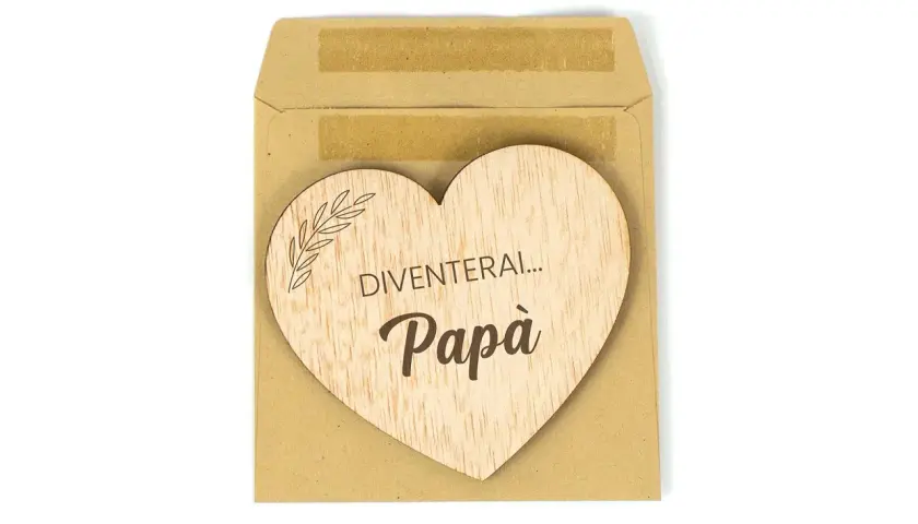 Cuore di legno con scritta "Diventerai... Papà", un dolce annuncio di gravidanza in una busta marrone.
