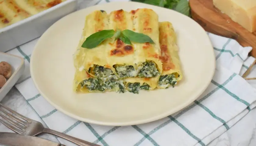 Pyszne cannelloni ze szpinakiem, zapieczone pod beszamelem i serem, ozdobione listkiem bazylii.