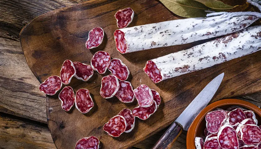 Tranches de saucisson sec, entiers et coupés, sur une planche en bois. On peut cuire du saucisson sec pour le déguster chaud.