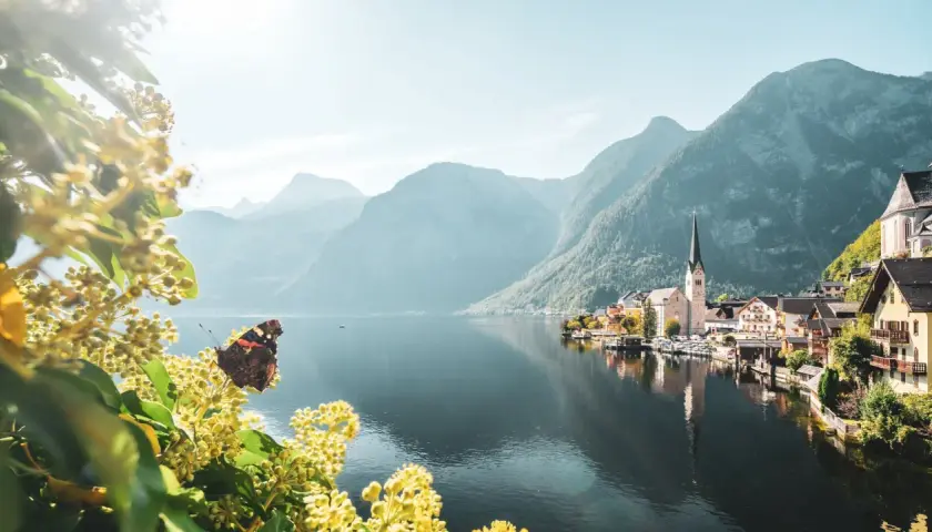 Schmetterling auf blühendem Zweig vor malerischem Dorf am See, umgeben von majestätischem Gebirge Europas.
