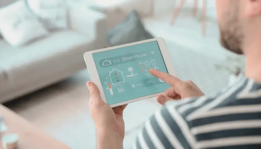 Un hombre controla su hogar inteligente desde una tablet, un vistazo a la historia de la domótica.