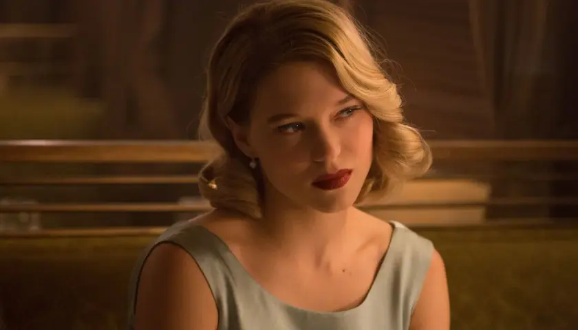 Léa Seydoux w eleganckiej sukience, z burzą blond włosów i czerwoną szminką, przypomina postać z jej filmów.