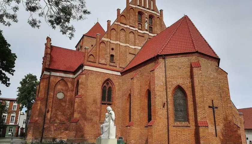 Majestatyczny kościół w Pucku z cegły, z czerwonym dachem i rzeźbą Matki Boskiej.