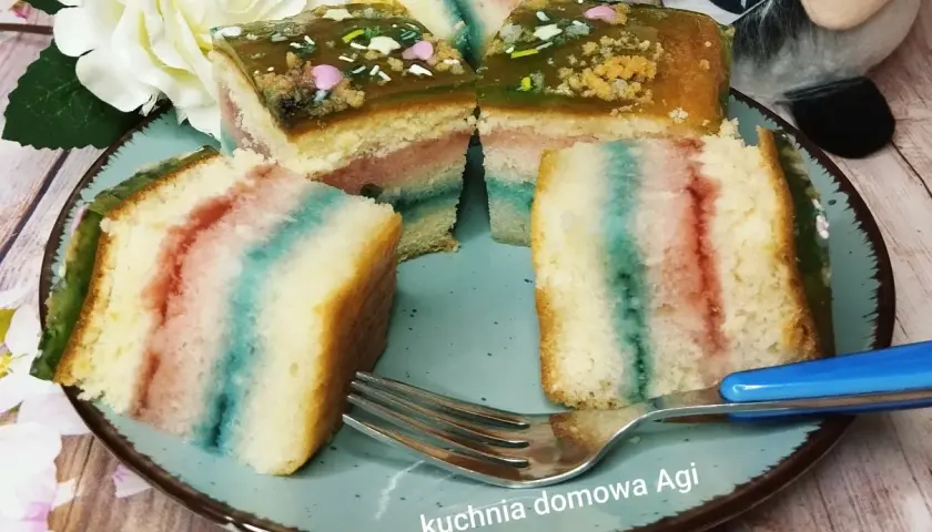 Kolorowy biszkopt z galaretką i posypką na talerzu, obok widelec.