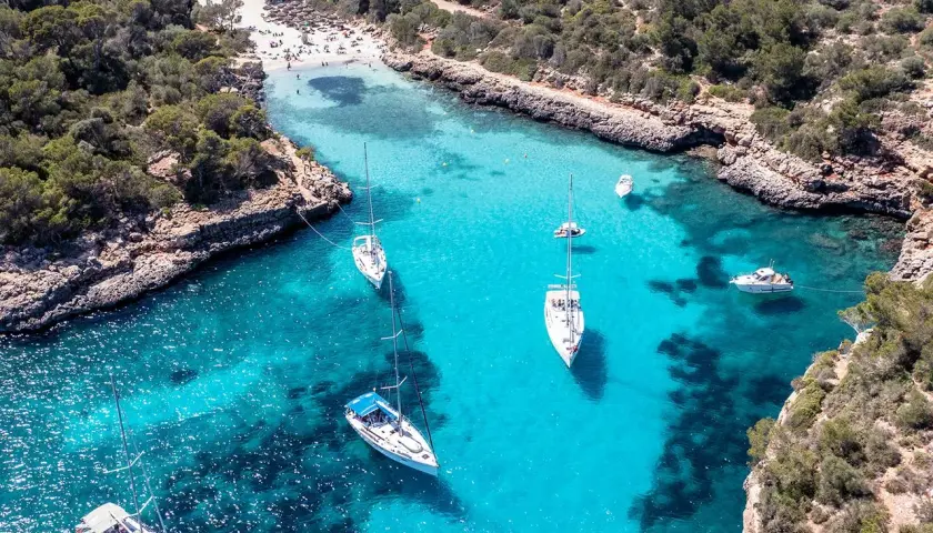 Traumhafte Bucht mit türkisfarbenem Wasser, Segelbooten und einem Strand – ein echter Mallorca Geheimtipp für unvergessliche Urlaubstage.
