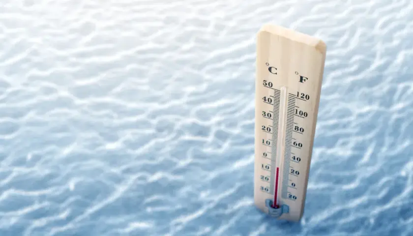Drewniany termometr pokazuje, że ile stopni ma Bałtyk w sierpniu, wskazując ok. 20°C. Woda jest lekko falująca.