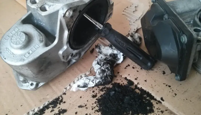 Zdemontowany zawór EGR Audi A4 B8 2.0 TDI z widocznymi objawami zanieczyszczenia sadzą. Narzędzie do czyszczenia.