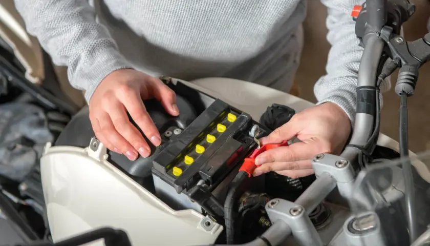 Ręce podłączają kable do akumulatora motocyklowego, szukając odpowiedzi, dlaczego akumulator się rozładowuje.