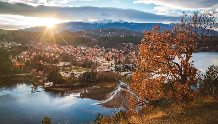 Widok na miasteczko nad jeziorem, góry w tle. Idealne miejsce, gdzie na wakacje w sierpniu, choć liście drzew już brązowe.