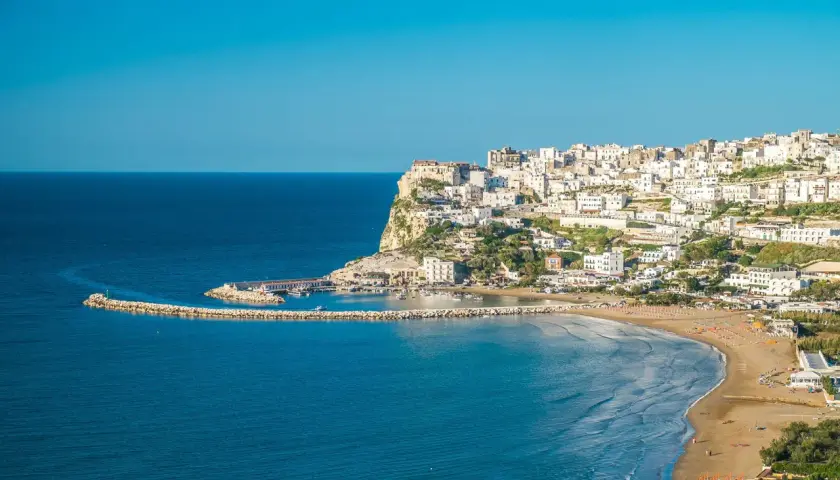 Vue panoramique de Peschici, Italie, avec ses maisons blanches perchées sur la falaise, sa plage de sable fin et son port pittoresque.