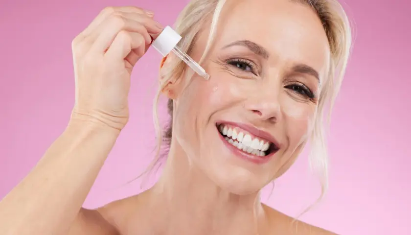 Glad kvinna applicerar serum, oroar sig inte för niacinamide biverkningar.