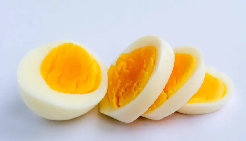 Ein halbes und drei Scheiben hartgekochtes Ei auf weißem Hintergrund. Ein Ei hat viel Protein.