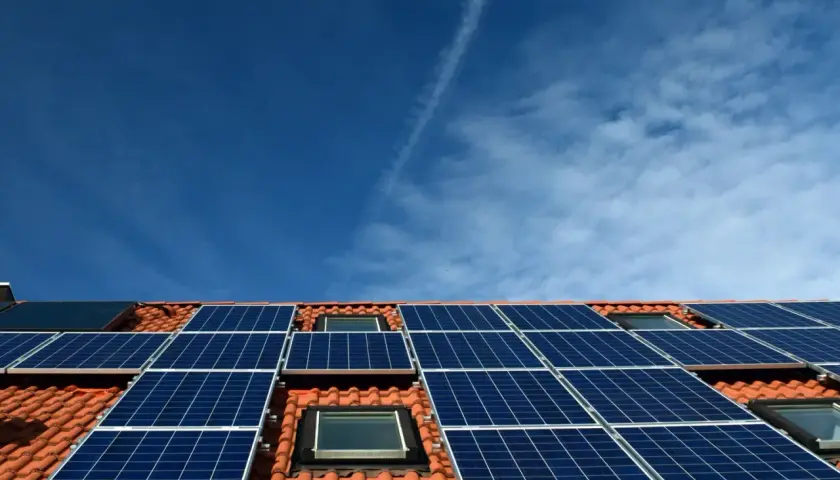Nowoczesna instalacja PV na dachu z dachówką, pod błękitnym niebem. Panele słoneczne zbierają energię.