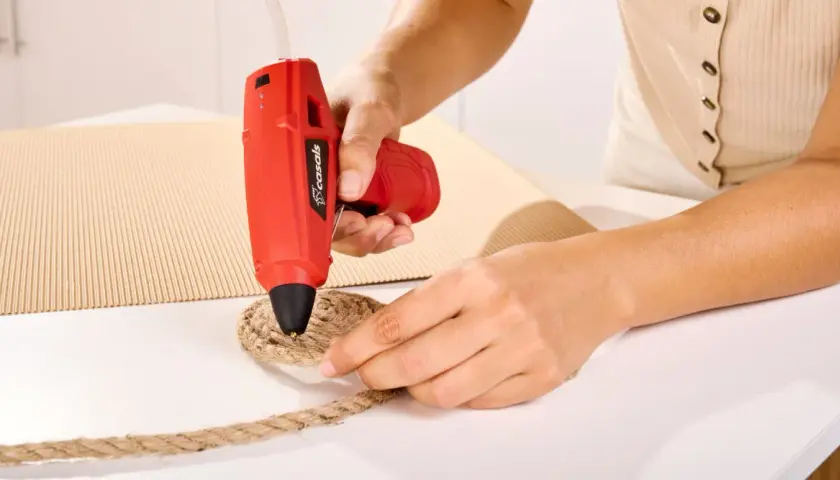 Persona usa pistola de silicona roja para pegar cuerda a cartón. Así es como funciona la pistola de silicona.
