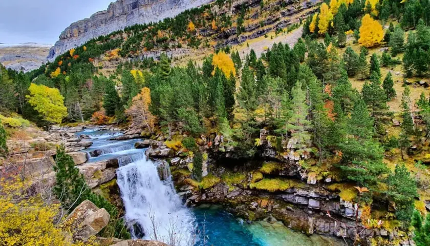 Cascada y río en la ruta Cola de Caballo, rodeados de bosques otoñales y montañas imponentes.