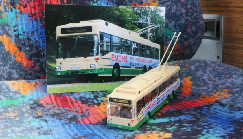 Ein Modell eines Obusses steht neben einer Fotografie eines echten Obusses. Beide zeigen die Aufschrift "EMONS DER GEBÄUDEDIENSTLEISTER".