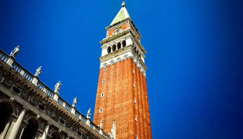 Le campanile de Venise se dresse fièrement sous un ciel bleu éclatant, orné de statues sur son flanc.