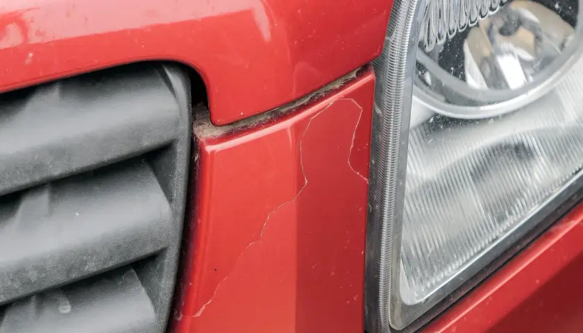 Pęknięty lakier na czerwonym zderzaku obok reflektora. Zastanawiasz się, ile kosztuje lakierowanie auta?