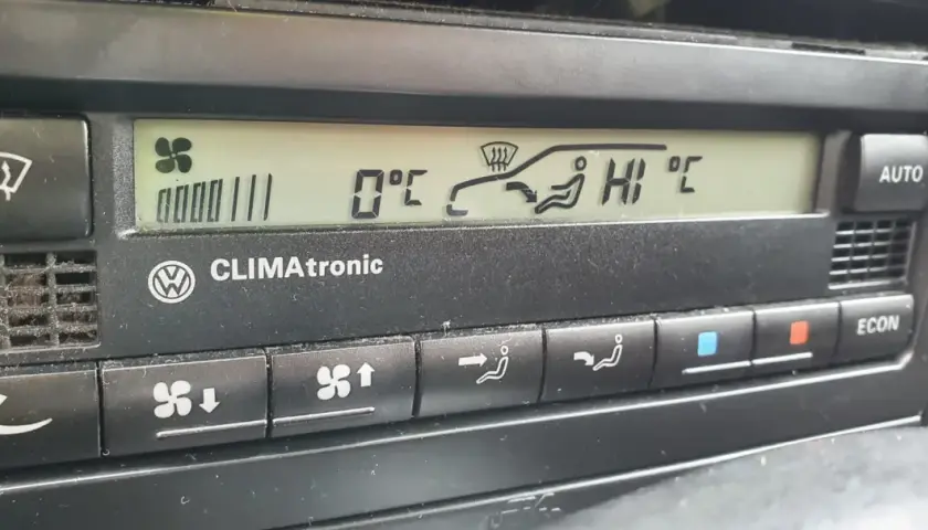 Panel klimatyzacji w samochodzie. Wyświetla 0°C, ikonę nawiewu na szybę i pasażerów, a także ustawienie "HI".