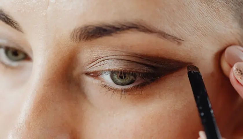 Application d'un fard brun pour comment maquiller des yeux verts. Un pinceau est utilisé pour définir la paupière.