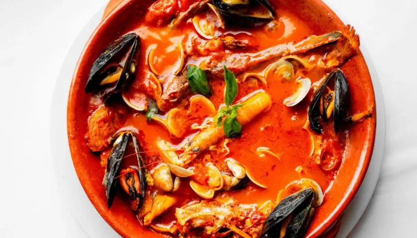 Un invitante brodetto di pesce in terracotta, ricco di cozze, vongole e gamberi, con un tocco di basilico fresco.