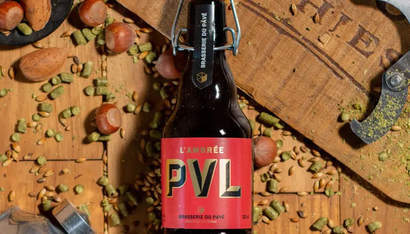 Bouteille de bière brune PVL, entourée de noisettes, de houblon et de grains. Une invitation à découvrir la recette biere brune.