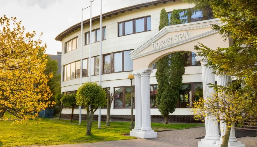 Elegancki budynek Doris Spa w Kołobrzegu z kolumnowym wejściem i kwitnącymi drzewami.