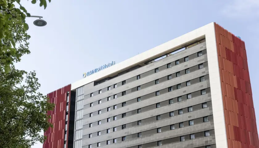 Edificio moderno con el logo "ILUNION Hotels" en la parte superior. Fachada gris con ventanas y detalles rojos.