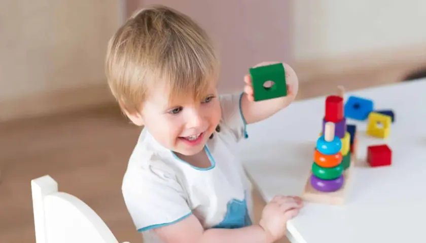 Bambino 3 anni sorridente gioca con blocchi colorati impilati.