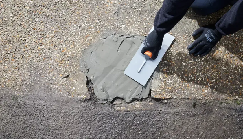 Rękawice i kielnia rozprowadzają zaprawę, wykonując naprawę betonu na zewnątrz.