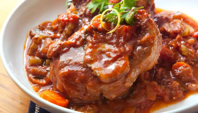 Herzhaftes Ossobuco Rezept in Tomatensoße mit Karotten und Petersilie, serviert in einer weißen Schüssel.