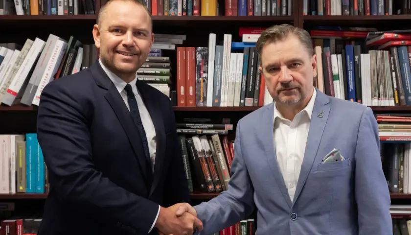 Dwóch mężczyzn w garniturach ściska sobie dłonie na tle regałów z książkami. Czy wybór Karola Nawrockiego na kandydata był konsultowany z Andrzejem Dudą?