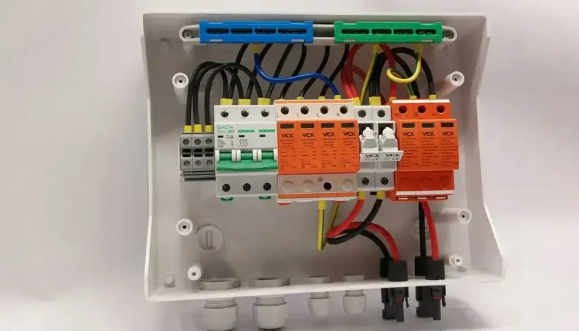Wnętrze białej obudowy, gdzie trwa budowa rozdzielni elektrycznej. Widoczne bezpieczniki, wyłączniki i zabezpieczenia przeciwprzepięciowe.