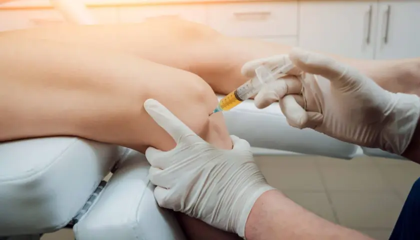 Lekarz wykonuje zastrzyk w kolano pacjenta. Zabieg iniekcji po polsku.
