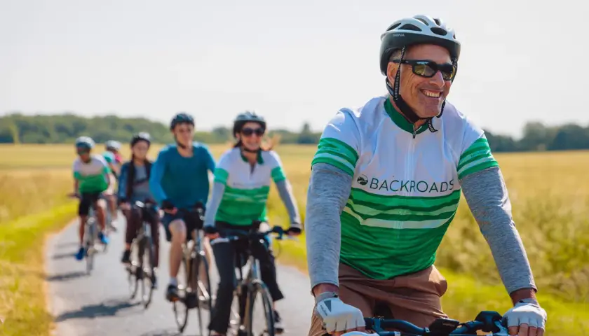 A group enjoys family cycling holidays on a sunny day, riding bikes down a paved path through golden fields.