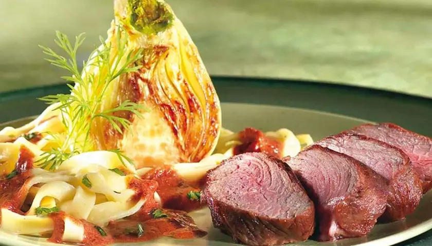 Tranches de rumsteak d'agneau rosé, accompagnées de pâtes fraîches, d'une sauce rouge et d'un fenouil braisé.