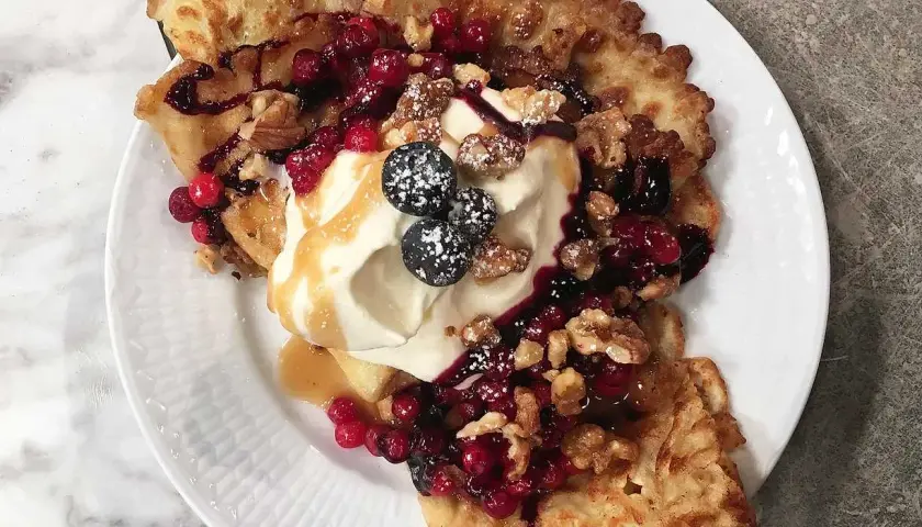 En härlig funnel cake toppad med vispgrädde, bär, nötter och sirap. En dröm för alla sötsugna!