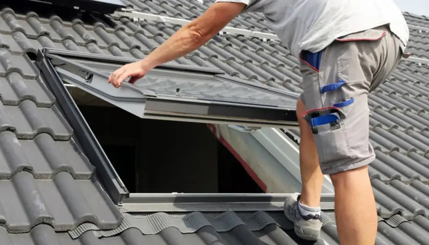 Hand führt ein Dachfenster ein, um es auf dem Ziegeldach zu montieren.