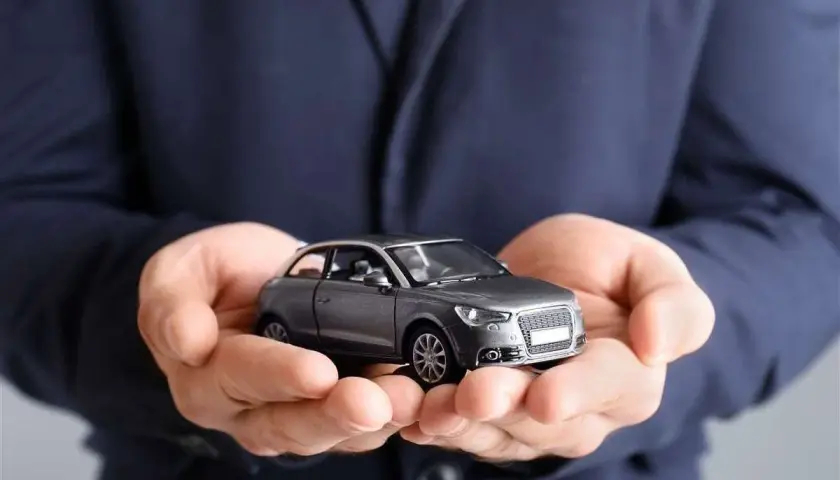Mani che sorreggono un modellino d'auto grigio. Non dimenticare la tua assicurazione scaduta 15 giorni fa!