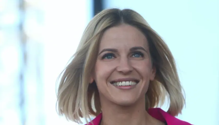 Uśmiechnięta Aleksandra Gajewska, której wykształcenie jest szeroko komentowane, w różowym żakiecie.
