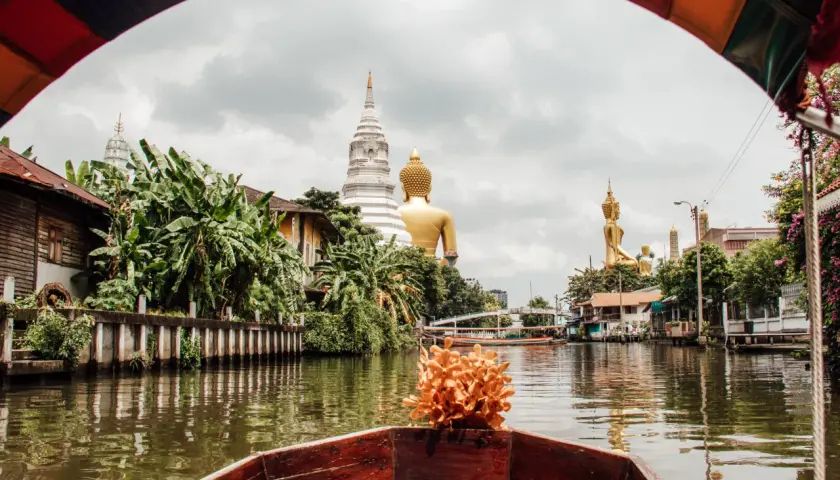 Bootsfahrt auf einem Kanal in Bangkok mit Blick auf goldene Buddha-Statuen und Tempel. Entdecken Sie diese Bangkok Geheimtipps abseits der ausgetretenen Pfade.