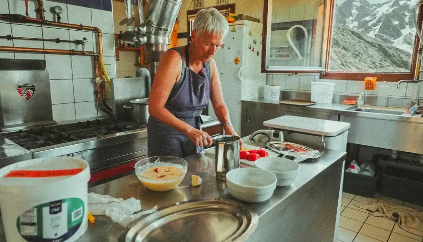 Une femme prépare des ingrédients dans une cuisine de montagne, un aperçu de son quotidien à travailler dans un refuge.