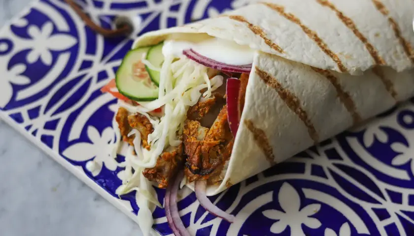 Pyszny kebab w picie z soczystym mięsem, chrupiącą surówką, pomidorem, ogórkiem i czerwoną cebulą, zawinięty w ciepły placek.