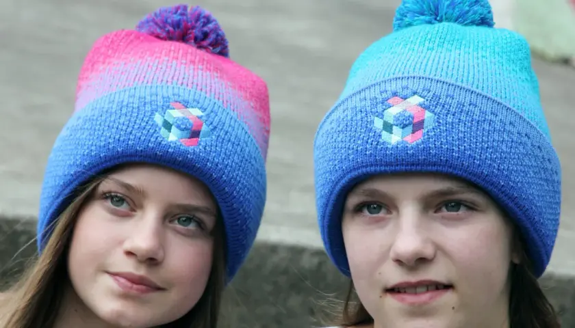 Zwei Mädchen mit bunten Bommelmützen in Blau und Pink.