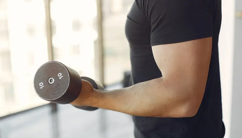 Mężczyzna wykonuje ćwiczenia na biceps z hantlem 10 kg. To jedne z najlepszych ćwiczeń na biceps.
